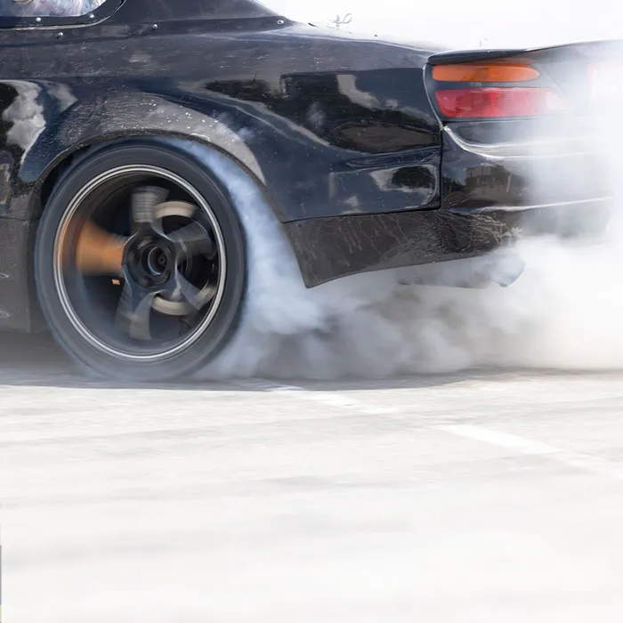 Heck eines schwarzen Auto beim Driften. Mit durchdrehenden qualmenden Reifen auf hellem Asphalt.