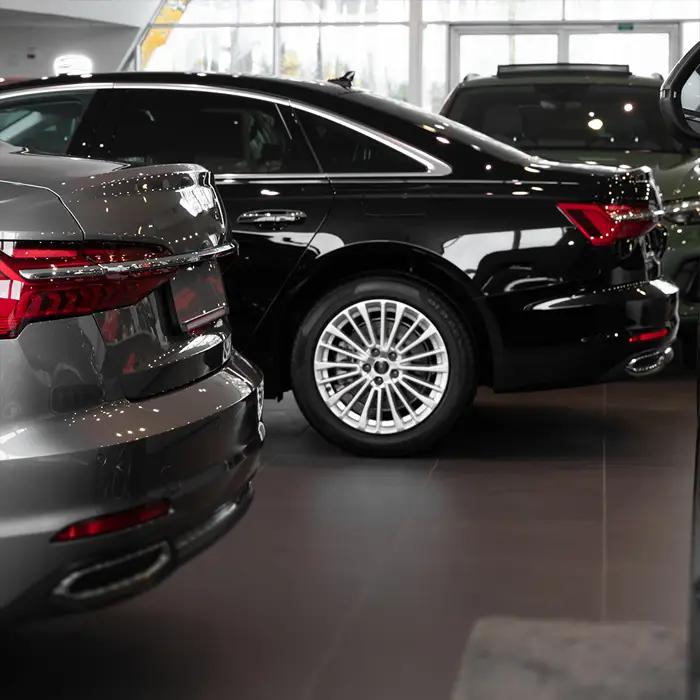 Im Ausstellungsraum eines Carsharing-Anbieters stehen mehrere Luxuslimousinen. Ein schwarzes Luxusauto mit großen Felgen steht in zweiter Reihe..Die Deckenbeleuchtung der Halle spiegelt sich auf dem Lack.