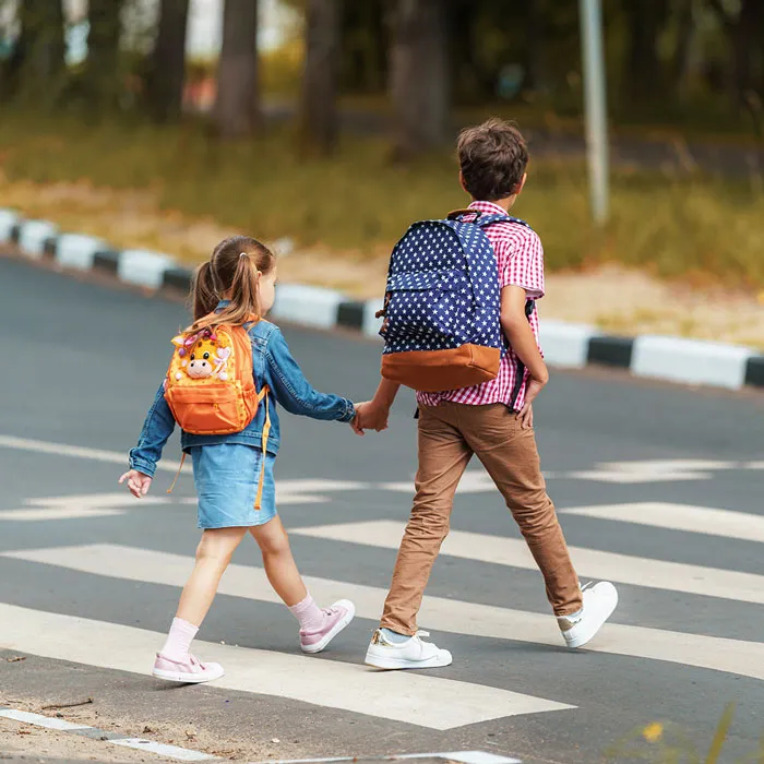 Zwei KInder gehen auf einem Zebrastreifen über die Strasse. Der Junge hält das kleinere Mädchen dabei sicher an der Hand.