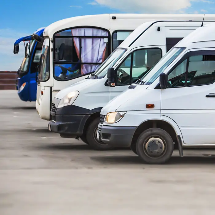 Auf einem Parkplatz stehen ein Camper, ein Wohnmobil und zwei Busse in einer Reihe. Der letzte Bus ist Blau, während die anderen drei Fahrzeuge Weiß sind.