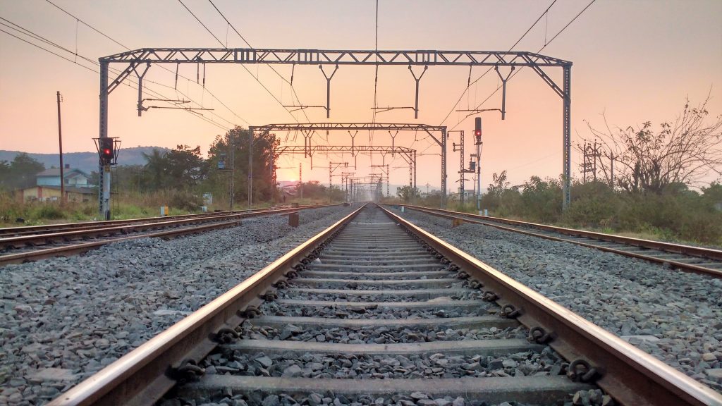 An leeren Eisenbahngleisen stehen Traversen, die die Oberleitungen für die Stromversorgung von Zügen halten. Zwei Lichtsignale stehen auf Rot.