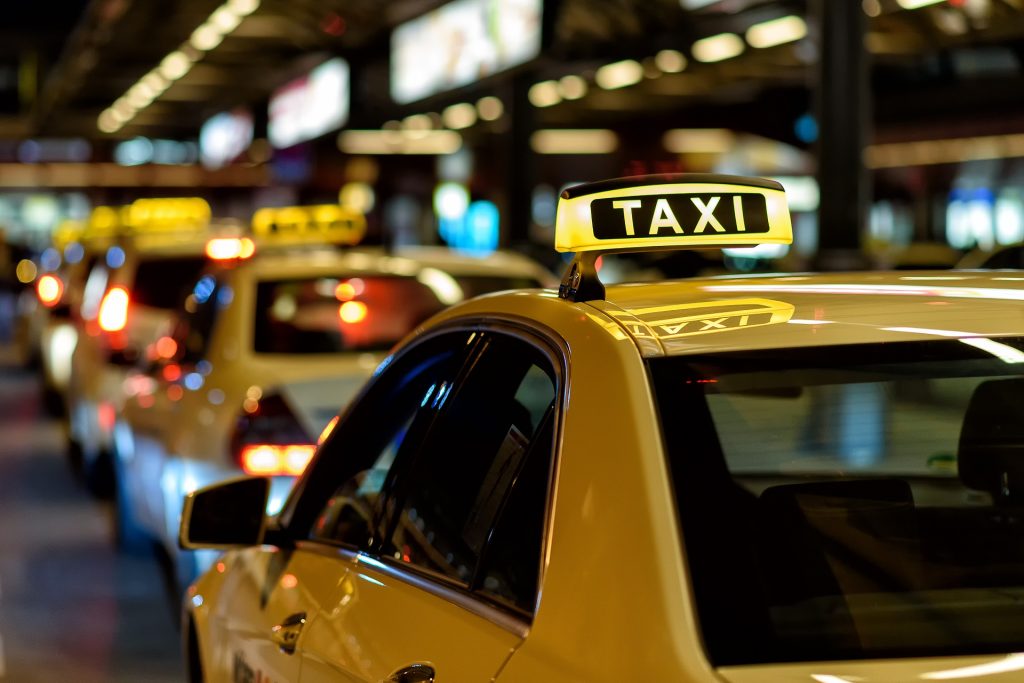 Viele Taxis stehen im Dämmerlicht in einer Reihe und warten auf Fahrgäste. Die Taxischilder auf den Dächern der beigefarbenen Autos leuchten, um ein freies Taxi zu signalisieren.