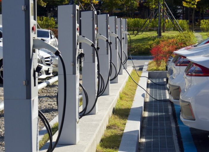 Auf einem Parkplatz stehen weiße Autos und eine Reihe Elektro-Ladesäulen. Zwei Fahrzeuge werden gerade aufgeladen.